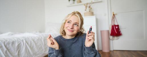 retrato do bonitinho, carismático beleza blogueiro, mulher senta dentro uma quarto com batom dentro mão, falando sobre inventar, conversando com seguidores, gravação conectados corrente em social meios de comunicação aplicativo foto