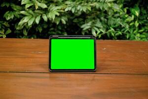 verde tela ipad ou tábua em de madeira mesa com verde plantas fundo foto