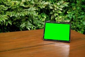 verde tela ipad ou tábua em de madeira mesa com verde plantas fundo foto