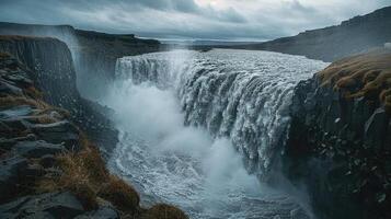 uma cascata é fluindo sobre uma penhasco debaixo uma nublado céu foto