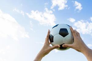 detém uma futebol bola dentro a céu em azul céu foto