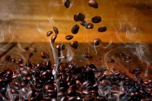 grãos de café torrados caindo na pilha, quentes e esfumaçados. fundo de madeira rústica desfocado foto