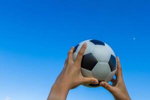 detém uma futebol bola dentro a céu em azul céu fundo. foto