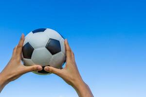 menina mão detém uma futebol bola dentro a céu em azul céu foto