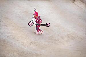 ativo desportivo criança dentro macacão passeios uma Rosa lambreta em a asfalto rastrear foto
