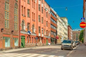 vista de uma rua vazia em helsínquia, finlândia. edifícios históricos coloridos com bandeiras finlandesas nas fachadas, carros estacionados e céu azul claro