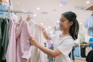 uma jovem menina é compras para roupas dentro uma loja foto