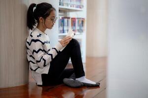 uma menina é sentado em a chão lendo uma livro foto