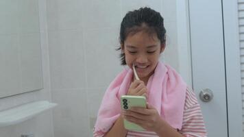 uma jovem menina é escovar dela dentes enquanto segurando uma célula telefone foto