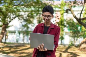 retrato do ásia Faculdade aluna usando computador portátil olhando para Câmera. uma homem trabalhando com uma computador portátil computador às campus foto