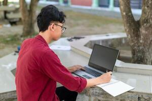 retrato do ásia Faculdade aluna usando computador portátil olhando para Câmera. uma homem trabalhando com uma computador portátil computador às campus foto