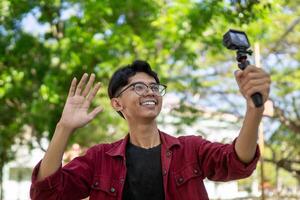 ásia homem gravação e falando para Câmera. jovem homem vlogging e levando selfie com açao Câmera às público parque. foto