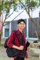 retrato do ásia Faculdade aluna com mochila sorridente para Câmera às a campus parque. foto