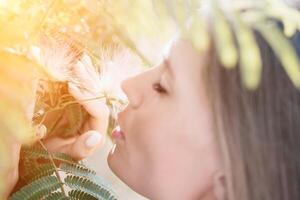 beleza retrato do feliz mulher fechar-se. jovem menina cheirando chinês acácia Rosa florescendo flores retrato do jovem mulher dentro florescendo primavera, verão jardim. romântico vibe. fêmea e natureza foto