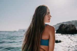 mulher mar e aí. fechar acima retrato do feliz jovem caucasiano mulher com grandes cabelo olhando às Câmera e sorridente. fofa mulher retrato dentro uma azul bikini posando em sup borda dentro a mar foto