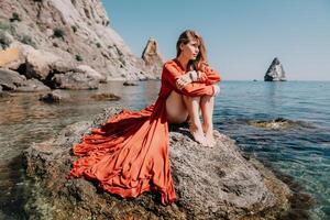 mulher viagem mar. feliz turista dentro vermelho vestir apreciar levando cenário ao ar livre para recordações. mulher viajante posando em a Rocha às mar baía cercado de vulcânico montanhas, partilha viagem aventura viagem foto