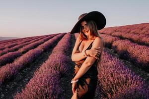 mulher lavanda campo. feliz despreocupado mulher dentro Preto vestir e chapéu com ampla borda caminhando dentro uma lavanda campo durante pôr do sol. perfeito para inspirado e caloroso conceitos dentro viagem e desejo de viajar. foto