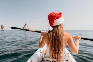 mulher dentro caiaque costas visualizar. feliz jovem mulher dentro santa chapéu flutuando dentro caiaque em calma mar. verão feriado período de férias e alegre fêmea pessoas relaxante tendo Diversão em a barco. foto