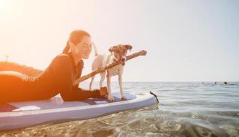 mar mulher e aí. silhueta do feliz positivo jovem mulher com dela cachorro, surfar em sup borda através calma água superfície. idílico pôr do sol. ativo estilo de vida às mar ou rio. verão período de férias com animais de estimação. foto