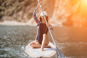 mulher sup ioga. meio era desportivo mulher praticando ioga pilates em remo sup prancha de surfe. fêmea alongamento fazendo exercite-se em mar água. moderno Individual fêmea hipster ao ar livre verão esporte atividade. foto