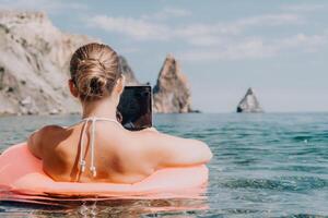 mulher trabalhador autonomo trabalho em computador portátil natação dentro mar em Rosa inflável anel. feliz turista dentro oculos de sol flutuando em inflável rosquinha e trabalhando em computador portátil computador dentro calma oceano. controlo remoto trabalhando qualquer lugar foto