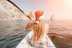 mulher dentro caiaque costas visualizar. feliz jovem mulher dentro santa chapéu flutuando dentro caiaque em calma mar. verão feriado período de férias e alegre fêmea pessoas relaxante tendo Diversão em a barco. foto