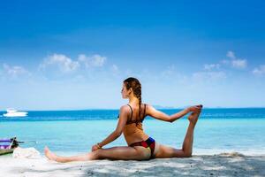 jovem mulher fazendo ioga exercícios em a mar de praia foto