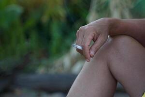 ásia do homem mão detém uma aceso cigarro e senta sozinho fumar dentro a fumar canto do dele casa. foto