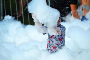 feliz pequeno Garoto com espuma em dele cabeça, dentro molhado roupas às uma espuma festa foto