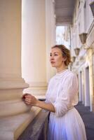 elegante meio era mulher dentro branco vintage vestir perto teatro com Antiguidade colunatas foto