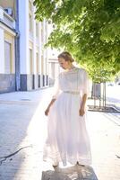 elegante meio era mulher dentro uma branco vintage vestir contra a fundo do histórico edifícios dentro a manhã luz foto