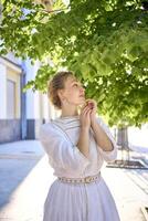 elegante meio era mulher dentro uma branco vintage vestir contra a fundo do histórico edifícios dentro a manhã luz foto