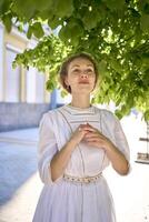 elegante meio era mulher dentro uma branco vintage vestir contra a fundo do histórico edifícios dentro a manhã luz foto