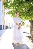 elegante meio era mulher dentro uma branco vintage vestir contra a fundo do histórico edifícios dentro a manhã luz foto