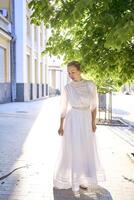 elegante meio era mulher dentro uma branco vintage vestir contra a fundo do histórico edifícios dentro a manhã luz foto