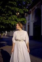 elegante meio era mulher dentro uma branco vintage vestir contra a fundo do histórico edifícios dentro a manhã luz foto