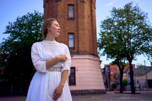 chique jovem mulher dentro uma branco vintage vestir em a quadrado perto a histórico água torre dentro vinnytsia foto