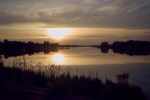 uma homem dentro uma caiaque dentro a meio do uma lago às pôr do sol foto