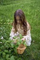 uma pequeno menina com grandes cabelo coleta flores dentro a Páscoa cesta foto