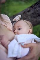 lindo mãe é amamentação dela bebê menina dentro a jardim foto