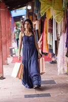senhora caminhando dentro azul vestir segurando compras bolsas enquanto caminhando dentro sarojini mercado Délhi foto