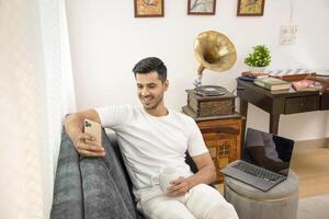 fofa homem segurando caneca dentro mão enquanto rolagem em Móvel telefone foto