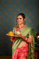 imagem do adorável mulher dentro saree segurando uma karwa Chauth pooja prato dentro mão foto