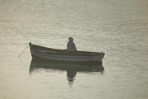 pescador às alvorecer dentro pescaria barco foto