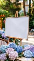 uma branco em branco horizontal poster em cavalete dentro frente do Casamento recepção mesas com pastel azul e roxa cores hortênsia flores foto