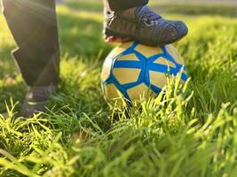 crianças pé do a vencedora dentro a velho Esportes sapatos tênis carrinhos em uma futebol bola contra uma fundo do grama. fechar-se rua tiro do jogos e Treinamento com vitória. foto