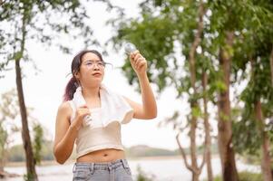 uma mulher detém uma pequeno ventilador enquanto em pé ao ar livre dentro uma parque, resfriamento ela mesma baixa em uma quente dia. foto