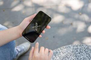 uma fechar-se tiro do uma mulher usando a x inscrição em dela Iphone enquanto sentado ar livre. foto
