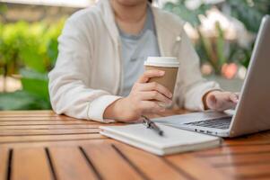 a ásia mulher trabalhando remotamente às uma cafeteria, bebericando café enquanto trabalhando em dela computador. foto