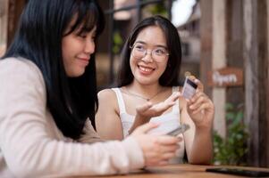 dois feliz ásia fêmea amigos estão falando sobre a benefícios do seus crédito cartões às uma cafeteria. foto